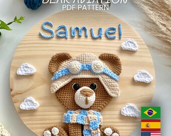Puede incluir: Placa de madera con un oso de ganchillo con gorro y bufanda de piloto. El nombre "Samuel" está escrito en hilo azul sobre el oso. El texto "BEAR AVIATION PDF PATTERN" está en la parte superior. Acentos de nubes blancas rodean al oso.