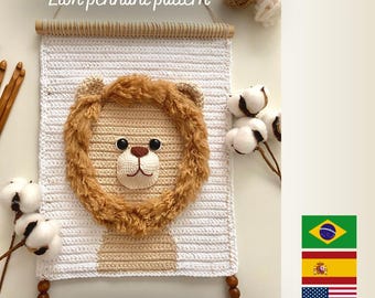 May include: A handmade crochet lion pennant pattern. The lion's face is centered on a white and tan rectangular background. The lion has a fluffy brown mane, black eyes, and a tan nose. The text "Lion pennant pattern" is at the top, and "PDF PATTERN" is at the bottom.