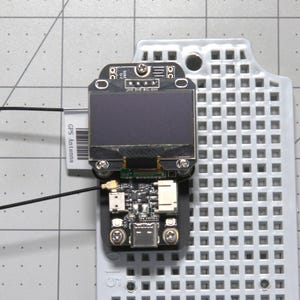May include: A black circuit board with a small LCD screen, a USB port, and a GPS antenna connector. The board is mounted on a gray pegboard.