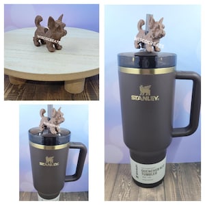 May include: A brown ceramic dog figurine with a straw in its mouth sits on top of a brown Stanley Quencher 40 oz Tumbler with a gold lid and handle. The tumbler has the Stanley logo and the words "Quencher 40 oz Tumbler" printed on it.