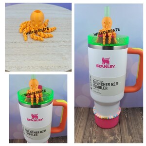 May include: Orange octopus-shaped straw topper with a green lid on a white Stanley Quencher H2.0 Tumbler with a pink base and colorful beads around the base.
