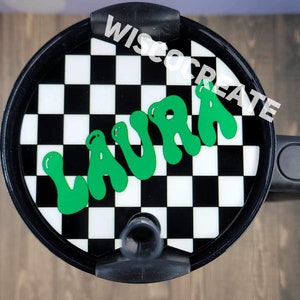 May include: Black and white checkered tumbler lid with a green "LAURA" name in a bubble font. The lid has a black straw hole and a black handle.