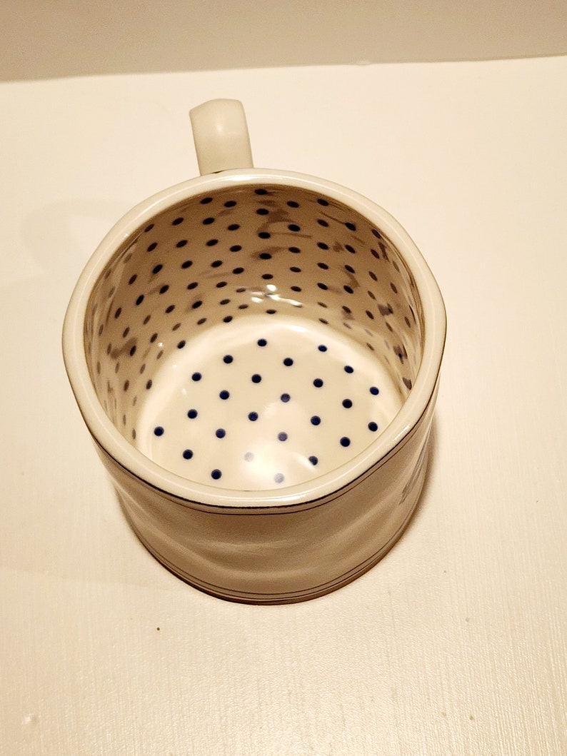 K&ouml;nnte beinhalten: Eine wei&szlig;e Rasierkelle aus Keramik mit Griff. Der Innenraum weist ein Muster aus blauen Punkten auf. Das &Auml;u&szlig;ere hat ein schlichtes Design mit einer d&uuml;nnen blauen Linie in der N&auml;he der Ober- und Unterseite.