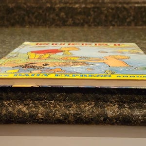 Puede incluir: La portada del libro anual del Daily Express de 1988 presenta una ilustraci&oacute;n colorida de una familia disfrutando de un d&iacute;a en la playa. La portada del libro es amarilla con el t&iacute;tulo "The Daily Express Annual" impreso en negro.