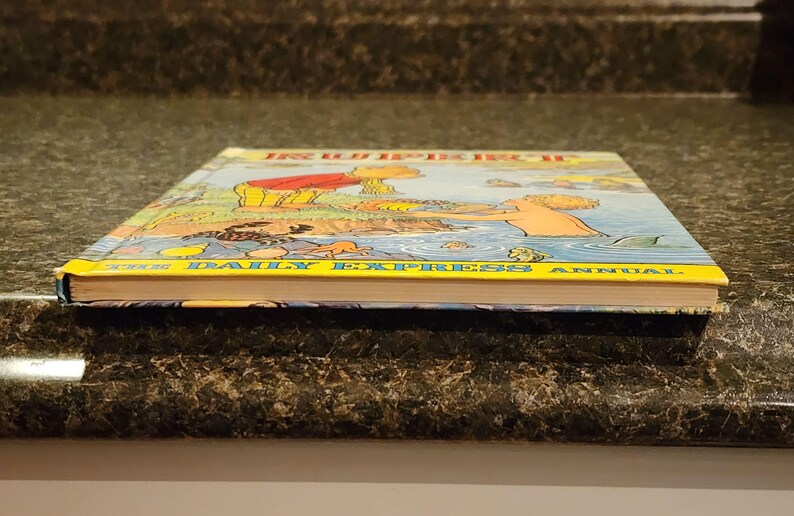 Puede incluir: La portada del libro anual del Daily Express de 1988 presenta una ilustraci&oacute;n colorida de una familia disfrutando de un d&iacute;a en la playa. La portada del libro es amarilla con el t&iacute;tulo "The Daily Express Annual" impreso en negro.