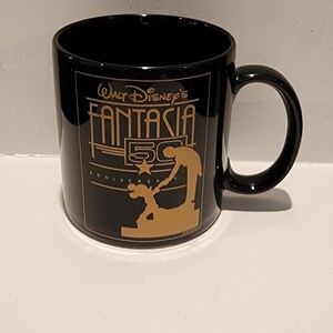 May include: Black ceramic coffee mug with a gold design featuring Mickey Mouse and the text "Walt Disney's Fantasia 50th Anniversary".