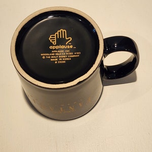 May include: Black ceramic coffee mug with a gold rim and the words "Disney's Universe" printed on the side. The bottom of the mug has a black and white label with the text "applause" and the words "The Walt Disney Company" and "Made in Korea".