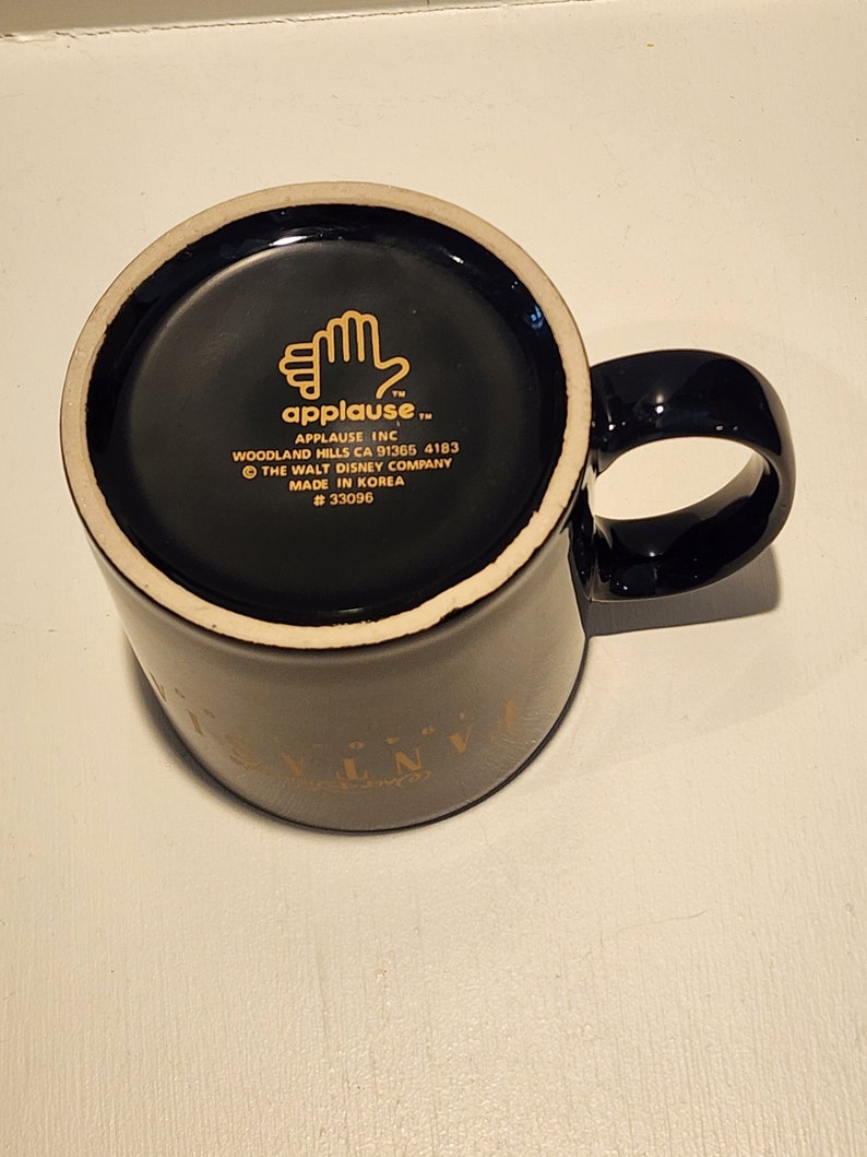 May include: Black ceramic coffee mug with a gold rim and the words "Disney's Universe" printed on the side. The bottom of the mug has a black and white label with the text "applause" and the words "The Walt Disney Company" and "Made in Korea".