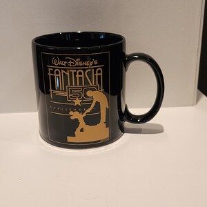 May include: Black ceramic mug with a gold design featuring Mickey Mouse and the text "Walt Disney's Fantasia 50th Anniversary".