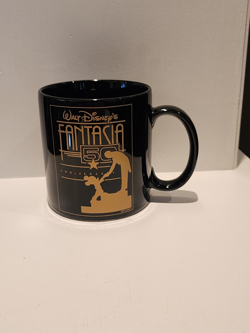 May include: Black ceramic mug with a gold design featuring Mickey Mouse and the text "Walt Disney's Fantasia 50th Anniversary".