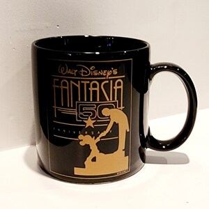 May include: Black ceramic coffee mug with a gold design featuring Mickey Mouse and Walt Disney's Fantasia 50th Anniversary logo.