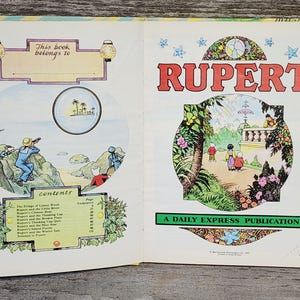 Puede incluir: Un libro infantil vintage titulado "Rupert: A Daily Express Publication" con una ilustraci&oacute;n colorida de un personaje de dibujos animados y una tabla de contenido que enumera varias historias. La portada del libro presenta un esquema de color verde, amarillo y azul con una etiqueta de precio de 2,95.