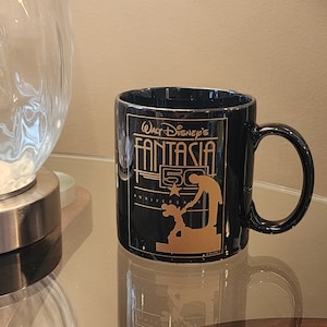 May include: Black ceramic coffee mug with a gold design featuring Mickey Mouse and the text "Walt Disney's Fantasia 50th Anniversary".