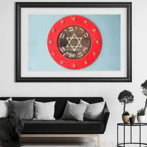 May include: A framed print of a red circle with a six-pointed star and Hebrew text. The circle is surrounded by a ring of metal studs.