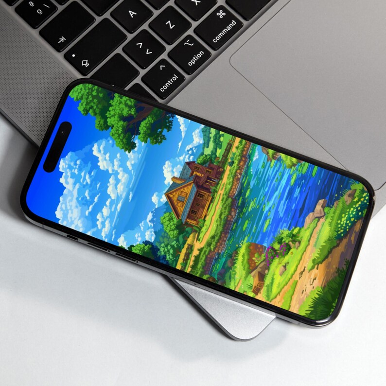 Op de afbeelding: Een smartphone met een levendige landschapssc&egrave;ne met een huis, rivier en bomen. De telefoon ligt op een zilveren draadloze oplader, in de buurt van een laptoptoetsenbord. Het scherm toont een kleurrijke, cartoonachtige illustratie.