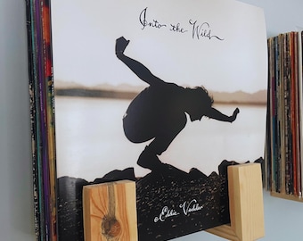 May include: A set of vinyl records with a wooden record holder. The record cover features a silhouette of a person jumping into the water with the text "Into the Wild" and "Eddie Vedder" written on it.