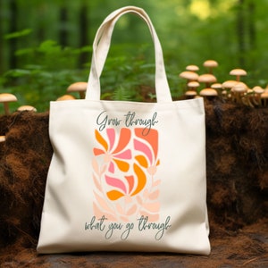 May include: A white canvas tote bag with a floral design and the text "Grow through what you go through".