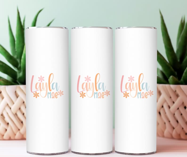 Op de afbeelding: Drie witte roestvrijstalen bekers met een bloemenmotief en de naam "Layla Mae" in pastelkleuren.