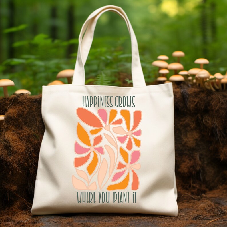 May include: A white canvas tote bag with the text "Happiness Grows Where You Plant It" and a colorful abstract floral design in shades of orange, pink, and peach.