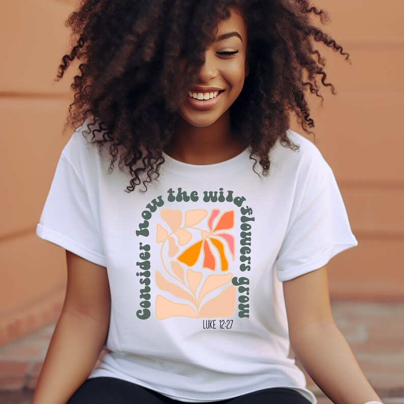 May include: White t-shirt with a graphic of colorful flowers and the text "Consider how the wild flowers grow" with the scripture reference "LUKE 12:27".