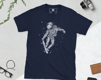 Puede incluir: Una camiseta azul marino con un gráfico de un astronauta haciendo skateboard en el espacio. El astronauta lleva un traje espacial y un casco, y la tabla de skate flota en el aire. El fondo es un cielo nocturno estrellado.