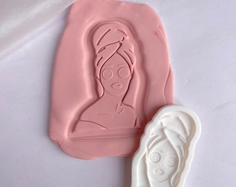 May include: White silicone mold of a woman with a towel on her head and cucumber slices on her eyes. The mold is used for making cookies, fondant, or other edible decorations.