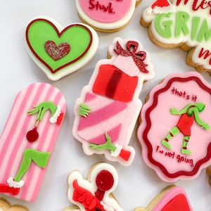 May include: A selection of Christmas-themed biscuits with festive designs. Includes heart-shaped biscuits, gift boxes, and Grinch-themed biscuits. Some biscuits feature text such as "Stink, Stark, Sturk" and "I'm not going."