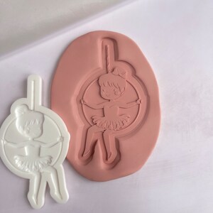 May include: A white silicone mould for baking or crafting. The mould features a design of a girl in a tutu swinging on a trapeze.