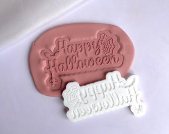 May include: A pink silicone mold with the words "Happy Halloween" and a spider web design. A white silicone mold with the same design is shown next to it.