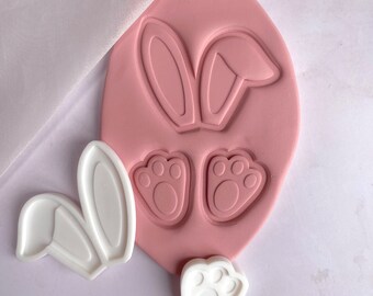 May include: Pink silicone mold with two bunny ear shapes and two paw print shapes. There are also three white silicone molds, one with two bunny ears and two with paw prints.