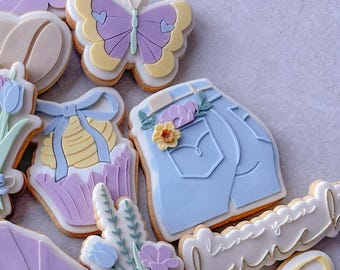 May include: Assortment of pastel-colored sugar cookies decorated with various designs, including a butterfly, a cupcake, a pair of jeans, flowers, and the text "love you bunch".