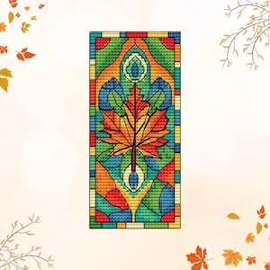 May include: A rectangular cross-stitch design featuring a colourful maple leaf. The leaf is rendered in shades of orange, yellow, and red, set against a background of green, blue, and yellow. The design has a stained-glass effect.