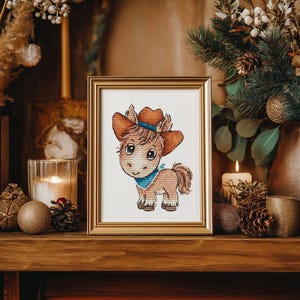 May include: A framed cross-stitch of a cartoon pony wearing a cowboy hat and a blue bandana. The pony is brown with a light brown mane and tail. The frame is gold, and the artwork is displayed on a wooden shelf with decorative items.