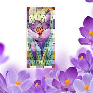 Pode incluir: Um padrão de ponto cruz de uma flor de croco roxo em estilo vitral. A flor é cercada por folhas verdes e um fundo azul.