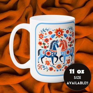 May include: White ceramic mug with a colorful floral design featuring two blue and red horses. The design is in a square frame with a blue border. The mug is 11 oz and says "11 oz size available!"