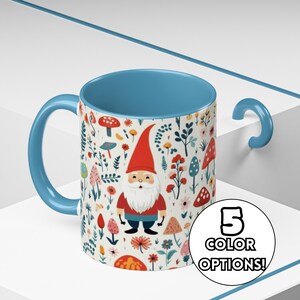 May include: A blue ceramic mug with a white background and a colorful pattern of gnomes, mushrooms, and flowers. The text "5 COLOR OPTIONS!" is printed on the right side of the mug.