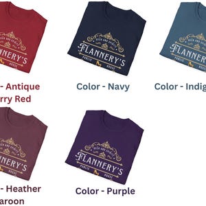 Pu&ograve; includere: Cinque magliette in vari colori: rosso ciliegia antico, blu navy, blu indaco, bordeaux erica e viola. Ogni maglietta mostra il testo "Flannery's Public House" in un design decorativo. Le magliette sono piegate e presentate su sfondo bianco.