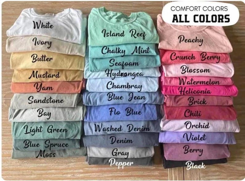 May include: A collection of folded t-shirts in various colors arranged in three vertical stacks. The text COMFORT COLORS ALL COLORS appears at the top right. The shirts are labeled with color names including White, Ivory, Butter, Mustard, Yam, Sandstone, Bay, Light Green, Blue Spruce, Moss, Island Reef, Chalky Mint, Seafoam, Hydrangea, Chambray, Blue Jean, Flo Blue, Washed Denim, Denim, Gray, Pepper, Peachy, Crunch Berry, Blossom, Watermelon, Heliconia, Brick, Chili, Orchid, Violet, Berry, and Black.