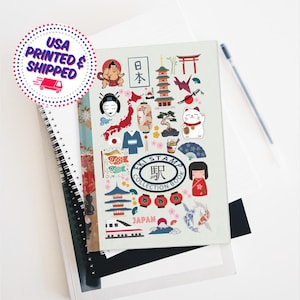 May include: A white notebook with a colorful design featuring Japanese cultural icons, including a red pagoda, a red torii gate, a white cat with a raised paw, a red and white carp streamer, and a red and white Japanese doll. The notebook has the text "EKI STAMP COLLECTION BOOK" in a black circle with white text. The text "JAPAN" is printed in black on a white background.