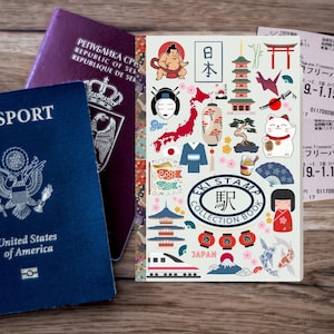 May include: A blue United States passport and a burgundy passport are next to a Japanese-themed notebook. The notebook features illustrations of sumo wrestlers, pagodas, and other Japanese cultural icons. Tickets are visible in the background.