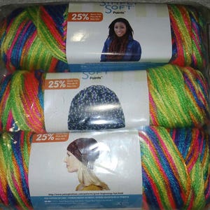 May include: Three skeins of Simply Soft Paints yarn in a clear plastic package. The yarn is a vibrant mix of colors including pink, green, blue, and orange. Each package has a label with a picture of a woman and a hat. The label also says "25% More Yarn".