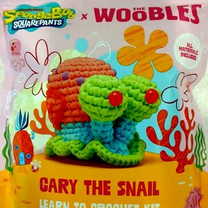 May include: A crochet kit featuring Gary the Snail from SpongeBob SquarePants. The kit includes all materials to learn crochet. The finished snail is orange, green, and blue, with red eyes. The packaging is pink and yellow.