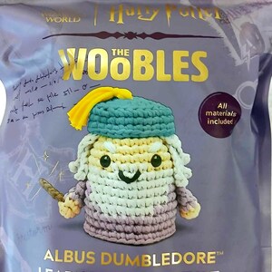 May include: A crochet kit featuring a character from the Harry Potter series. The kit includes all materials and is designed for beginners. The character is wearing a blue hat and yellow scarf, holding a wand. The kit is packaged in a purple bag.