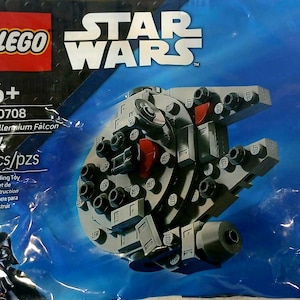 Puede incluir: Un juego de construcción LEGO Star Wars Millennium Falcon. El set incluye 74 piezas y está recomendado para mayores de 6 años. El modelo es gris con detalles negros y rojos, empaquetado en una bolsa de plástico azul.