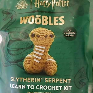 May include: A green bag with a Harry Potter The Woobles crochet kit. The kit includes all materials needed to crochet a Slytherin Serpent. The bag features a green snake and the text "All materials included".