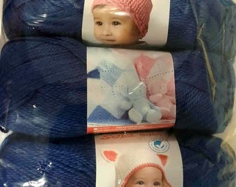 May include: Three skeins of blue Super Baby yarn. Each skein is wrapped in clear plastic and features a label with a baby wearing a knitted hat. The labels also show a knitted blanket and a teddy bear.