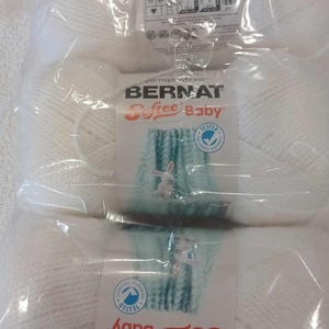 May include: Two packages of white Bernat Softee Baby yarn, each with a label featuring a blue and green crocheted blanket and a white bunny. The label also includes the text "Yarnspirations", "Bernat", "Softee Baby", and "Tested for harmful substances".