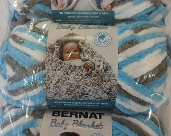 May include: Two skeins of Bernat Baby Blanket yarn in a blue, white, and gray striped pattern. The yarn is packaged in plastic and includes a free pattern for a baby blanket.
