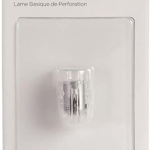 May include: A white package with a green Cricut logo and the text "Basic Perforation Blade" and "Lame Basique de Perforation". The package contains a clear plastic housing with a silver perforation blade inside. The text "For/Pour: Cricut Maker® QuickSwap™ Drive Housing" is printed on the bottom of the package.