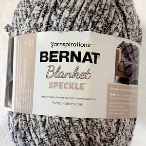 May include: A large ball of Bernat Blanket Speckle yarn in a speckled gray and white color. The yarn is labeled with the brand name and the words "Blanket Speckle". The label also includes the Yarnspirations logo and website.